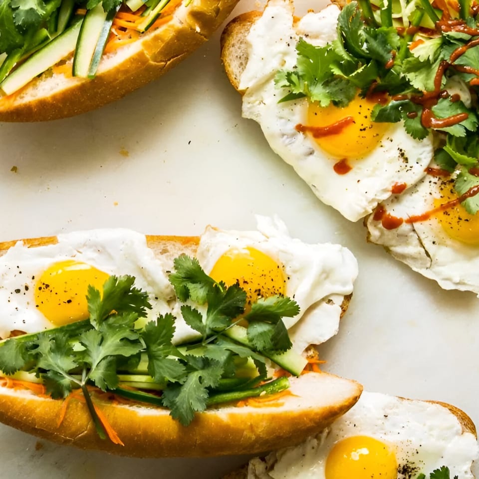 Three open-faced sandwiches with fried eggs, cilantro, and sliced vegetables on a white surface.