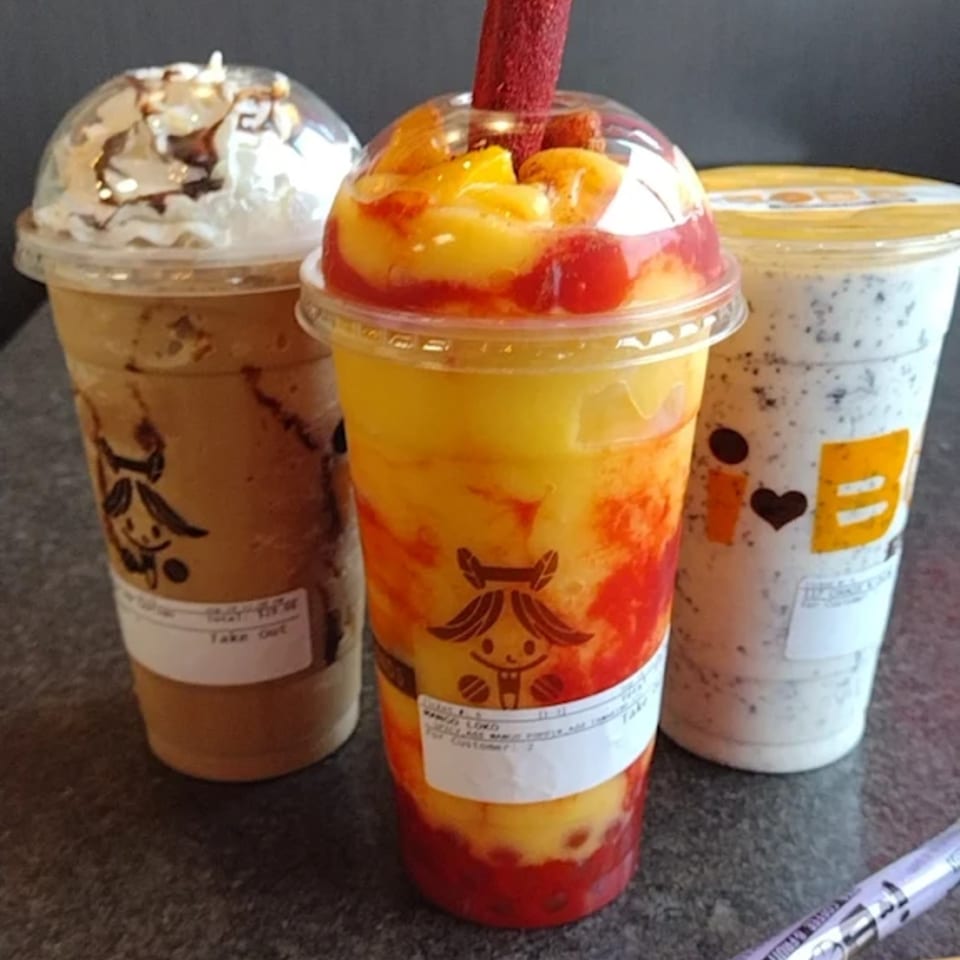 Three I HEART BOBA drinks: a coffee-colored drink with whipped cream, a mango and strawberry boba, and a cookies and cream boba.