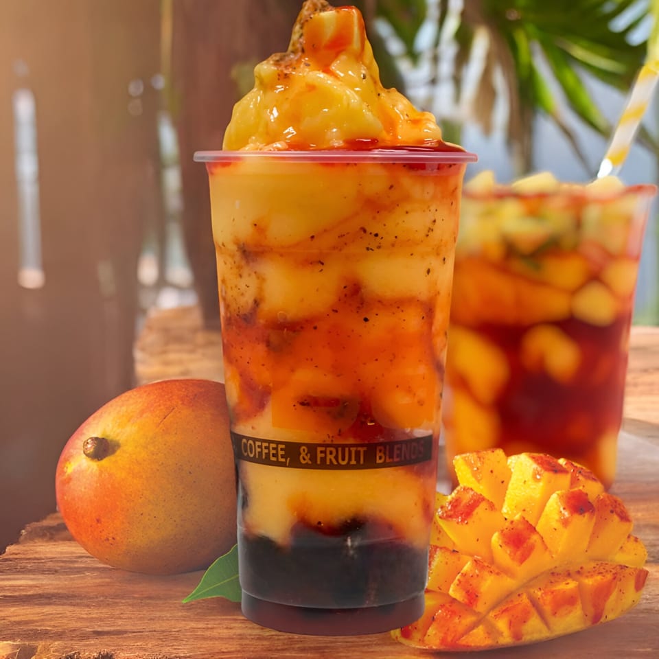 Two I HEART BOBA FM 529 mango drinks with fresh mangoes on a wooden surface.